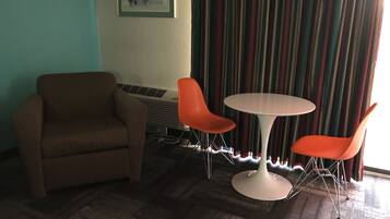 A room with a brown armchair, two orange chairs, a white table, and a striped curtain.
