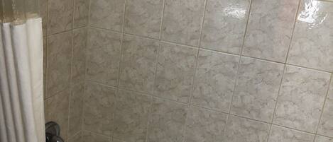 A bathroom with a bathtub, a showerhead, and a tiled wall.