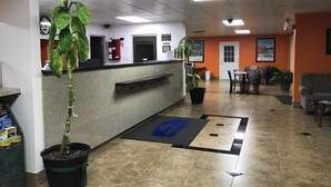 A reception area with a reception desk, a potted plant, a fire extinguisher, and a dining area with chairs and tables. - Howard Johnson by Wyndham Winter Haven FL (Winter Haven)