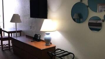 Habitación de hotel con escritorio, silla, lámpara, televisor y espejos en la pared.