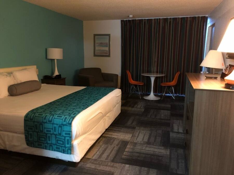 Ein Hotelzimmer mit einem Bett, einem Schreibtisch, zwei Stühlen, einer Lampe und einem Vorhang.