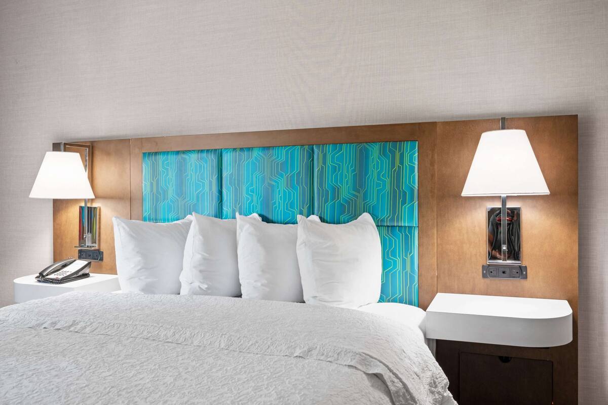Una camera d'albergo con un letto grande, biancheria da letto bianca, due lampade ai comodini, un telefono e uno specchio fissato alla parete.