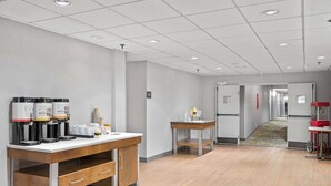 Un vestíbulo moderno de hotel con una estación de café, una recepción y un pasillo que conduce a otras habitaciones.