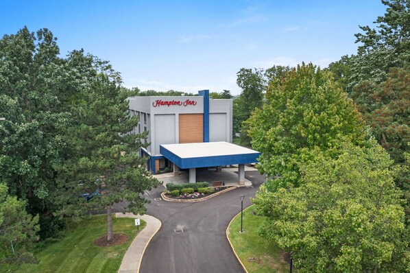 A Hampton Inn hotel with a modern design, featuring a prominent blue and white color scheme, surrounded by lush greenery.