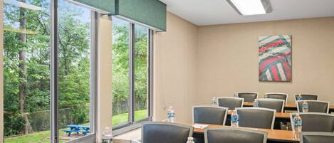 A conference room with large windows, a view of greenery, and a colorful abstract painting on the wall.