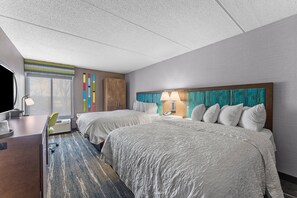 A hotel room with two beds, a desk, a chair, and a large window.