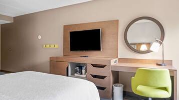 A hotel room with a bed, a desk with a chair, a television, a mirror, and a lamp.