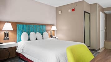 Una habitación de hotel con cama, mesitas de noche, un escritorio, una silla y una puerta.
