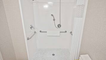 A walk-in shower with a white tiled floor, a handheld showerhead, a wall-mounted faucet, and a towel rack.