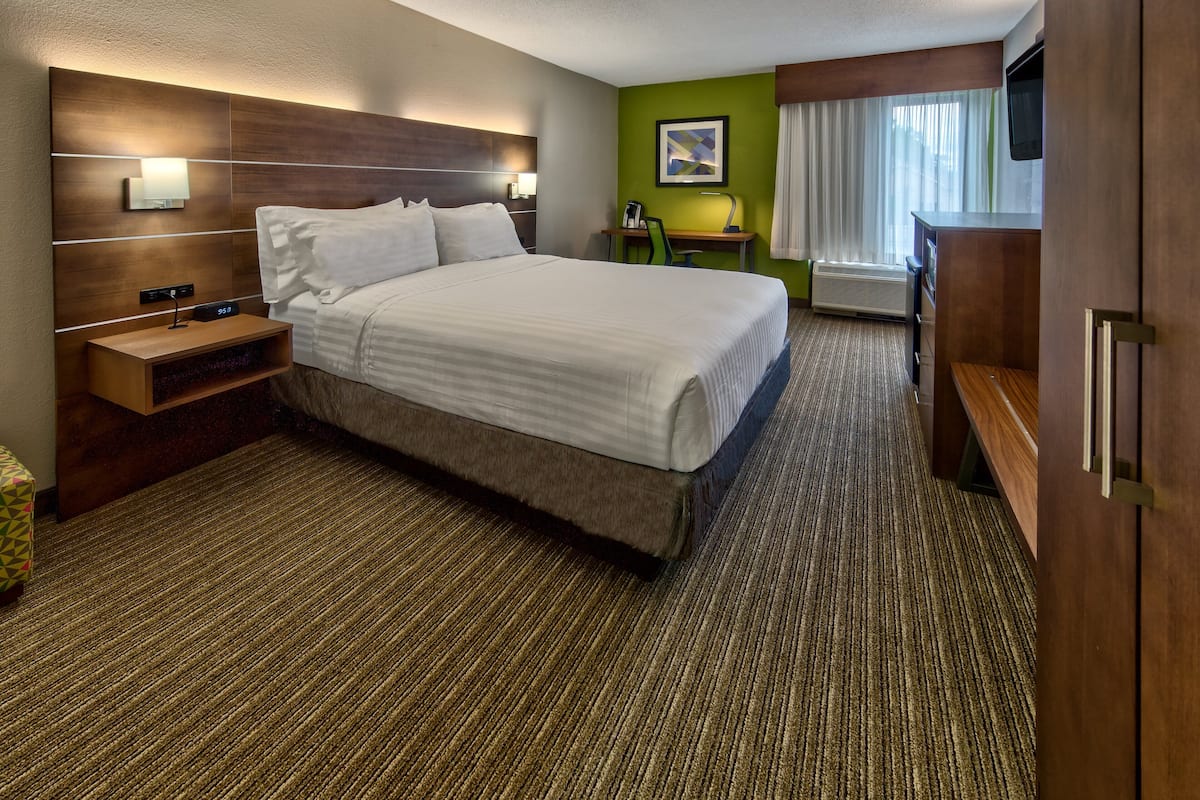 A hotel room with a large bed, a desk with a chair, a TV, and a small table with a lamp.