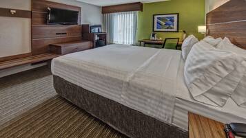 A hotel room with a large bed, a TV, a desk with a chair, a coffee maker, and a framed picture on the wall.