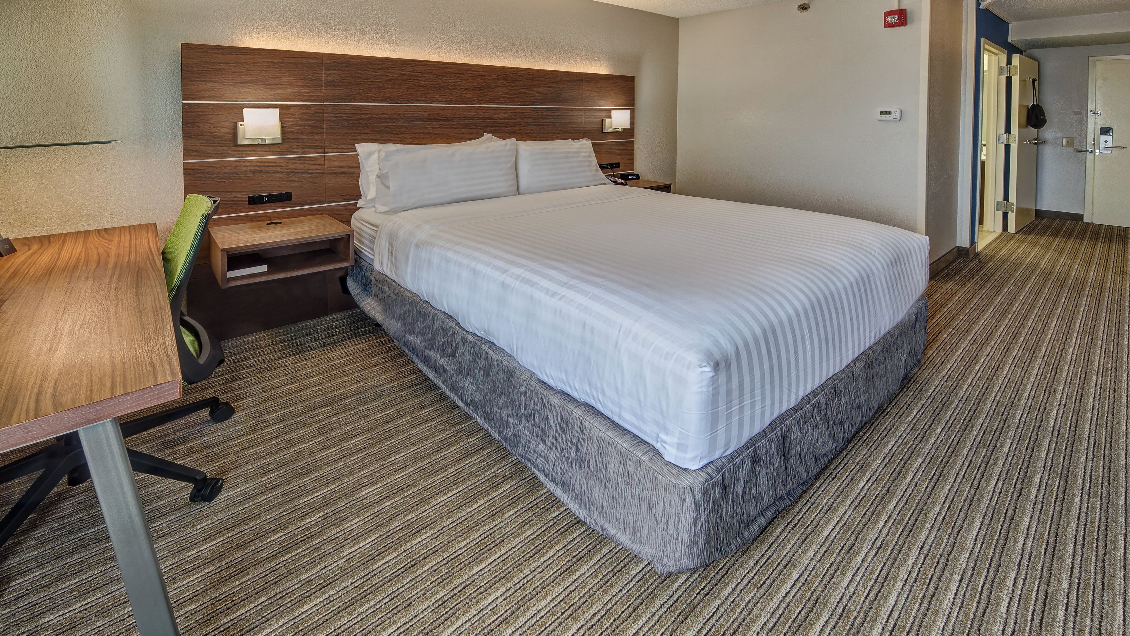 A hotel room with a bed, bedside table, lamp, and a chair.