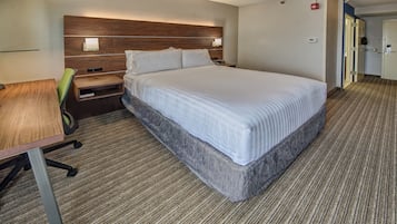 A hotel room with a bed, bedside table, lamp, and a chair.