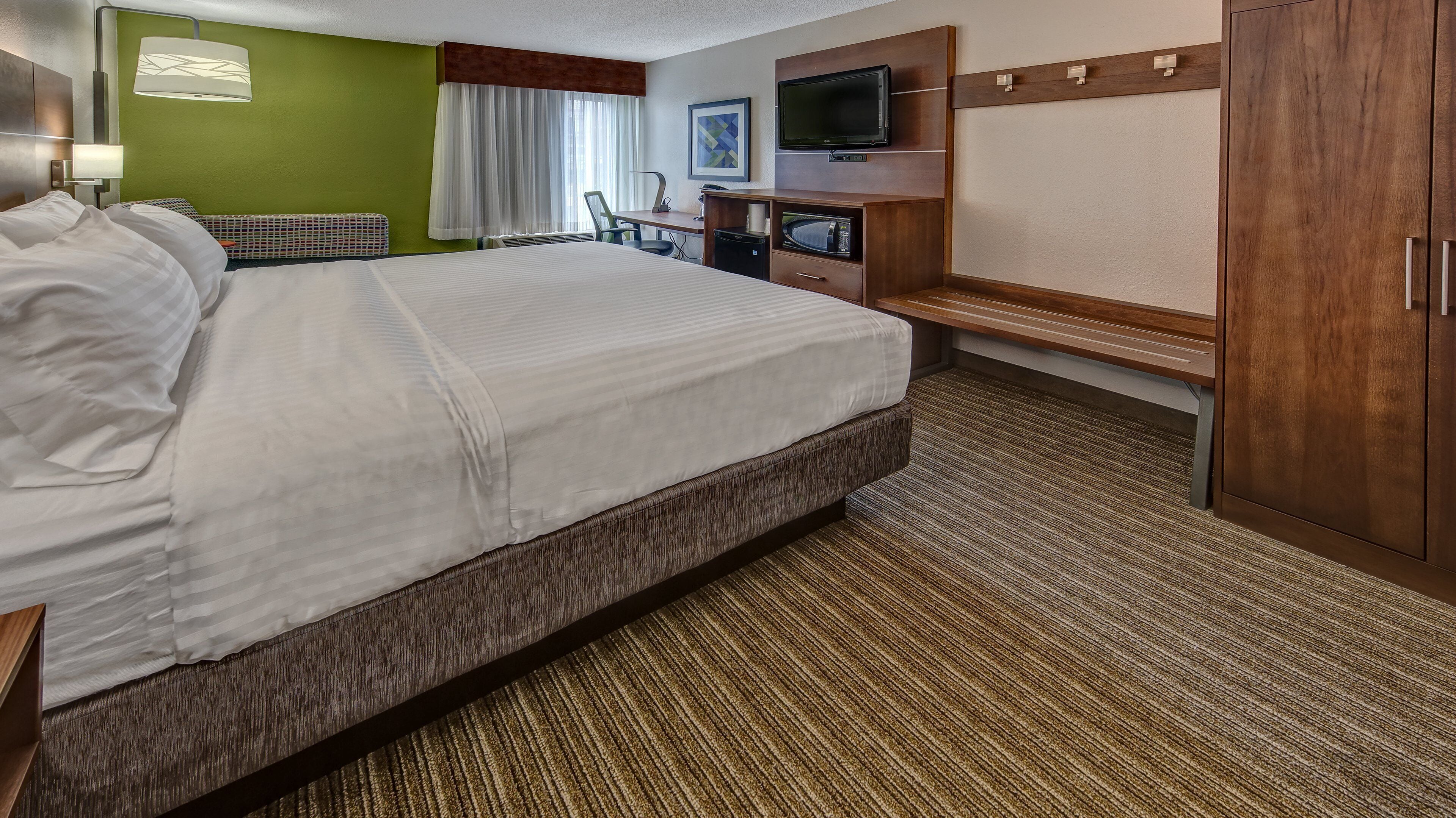 A hotel room with a large bed, a desk with a flat-screen TV, a microwave, and a wardrobe.