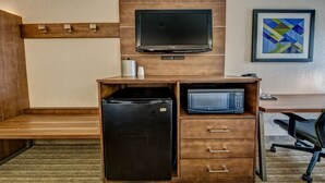 Una kitchenette compacta con refrigerador, microondas y un televisor de pantalla plana montado en la pared.