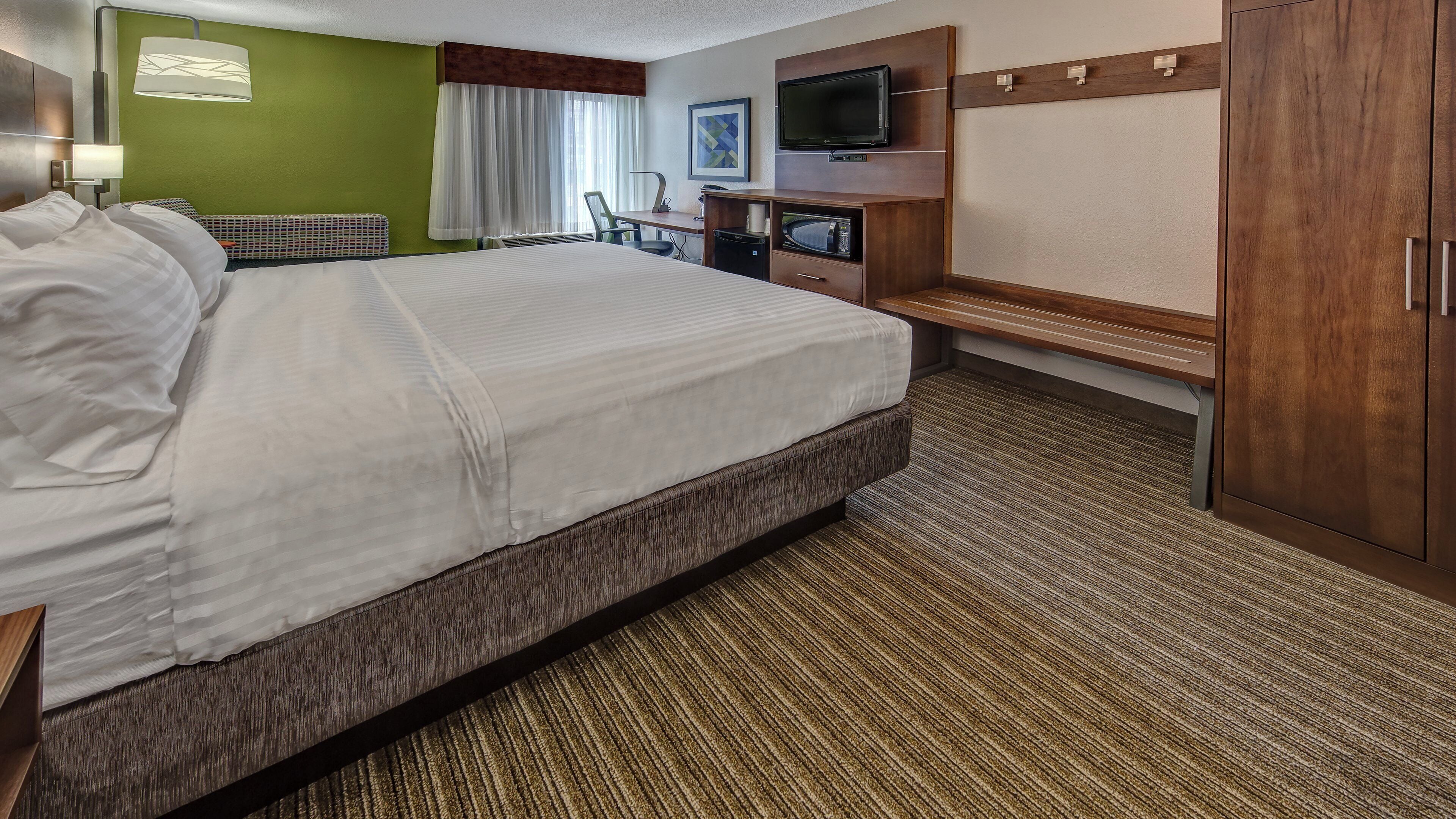 A hotel room with a large bed, a desk with a television, a microwave, and a wardrobe.