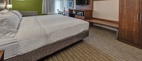 Una habitación de hotel con una cama grande, un escritorio con televisión, microondas y armario.