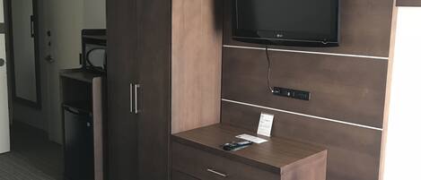 Habitación de hotel con una cama grande, un armario de madera, un televisor de pantalla plana montado en la pared y un escritorio pequeño con cajones.