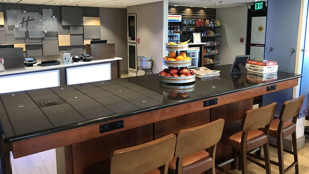 Zona de recepción de un hotel con mostrador, exhibición de frutas y un área de descanso con sillas.