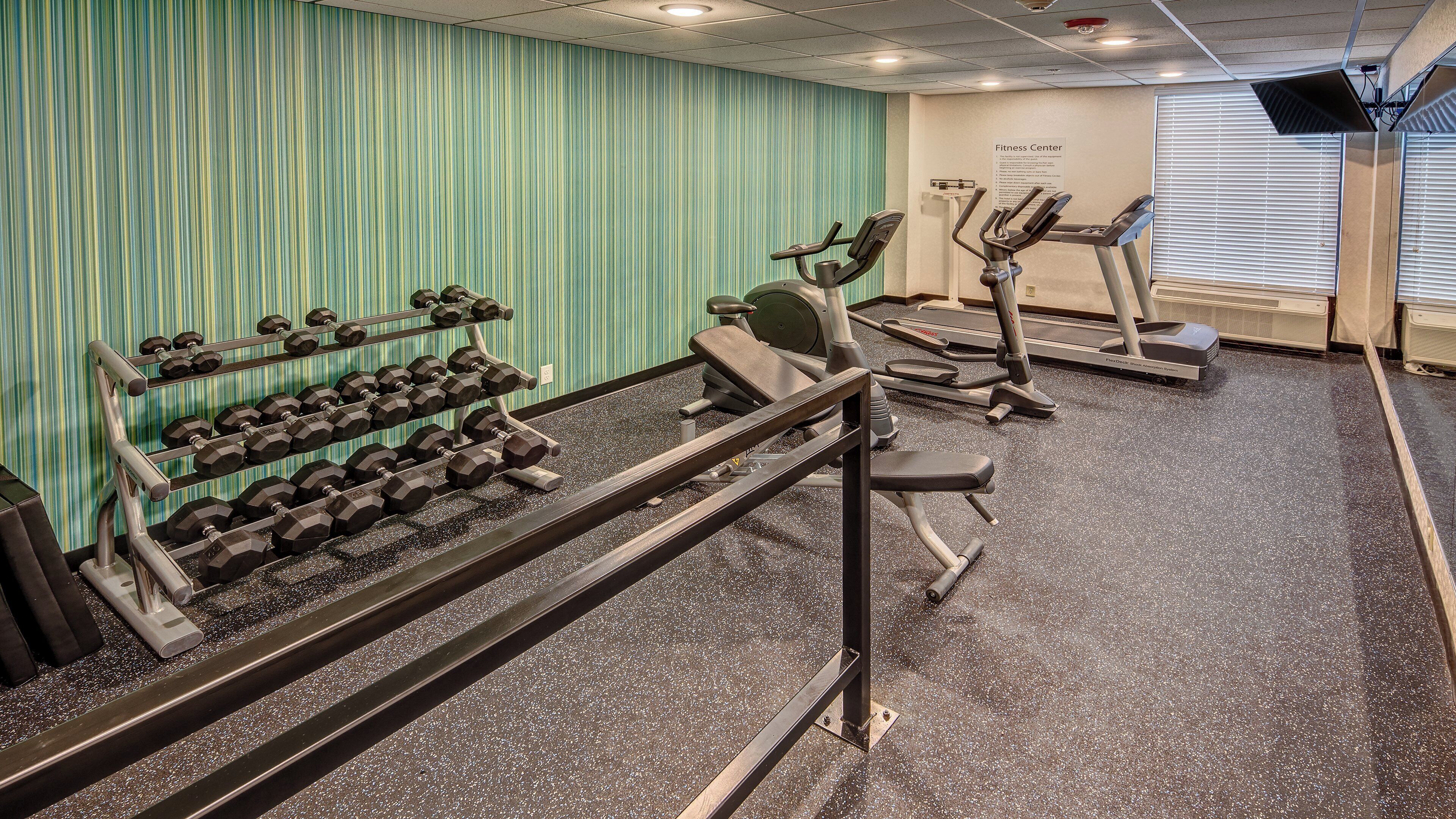 A fitness center with exercise equipment, including dumbbells, a bench press, and treadmills.