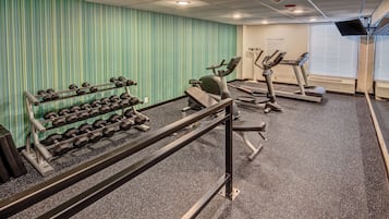 A fitness center with exercise equipment, including dumbbells, a bench press, and treadmills.