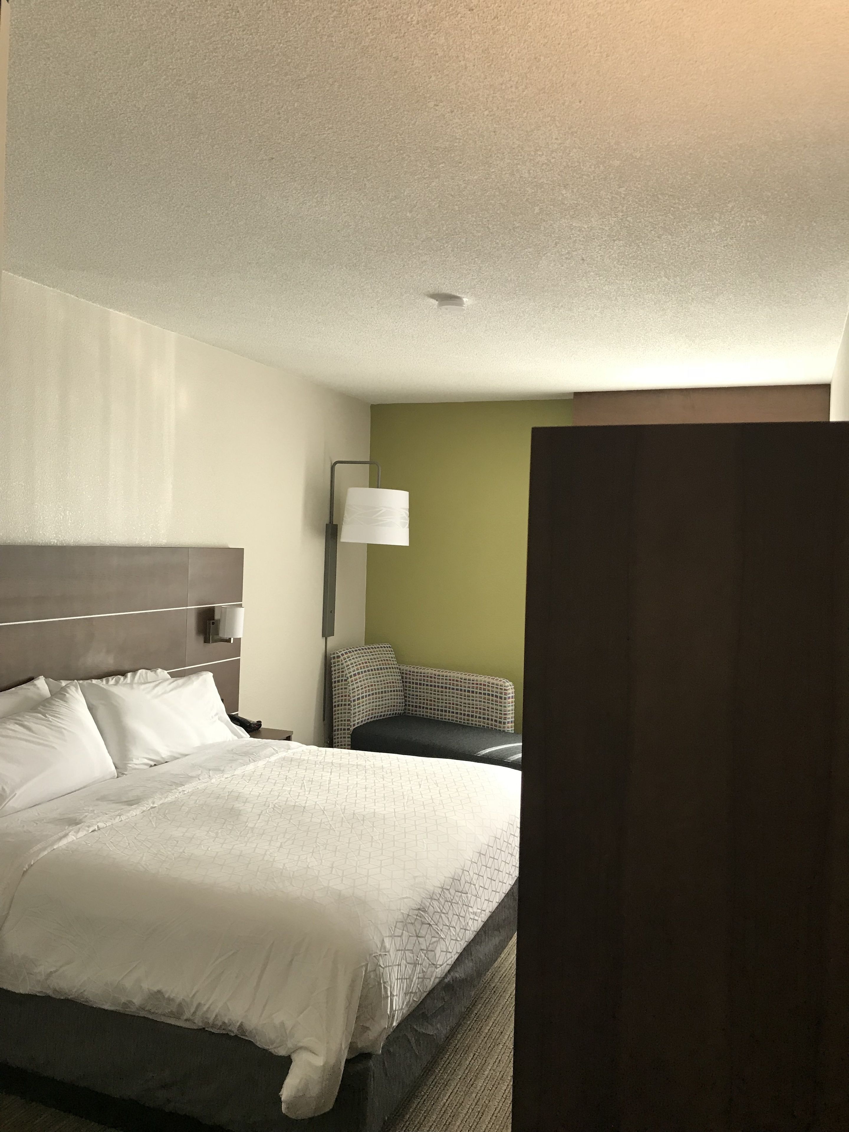 A hotel room with a bed, a nightstand, a lamp, and a wall-mounted light fixture.