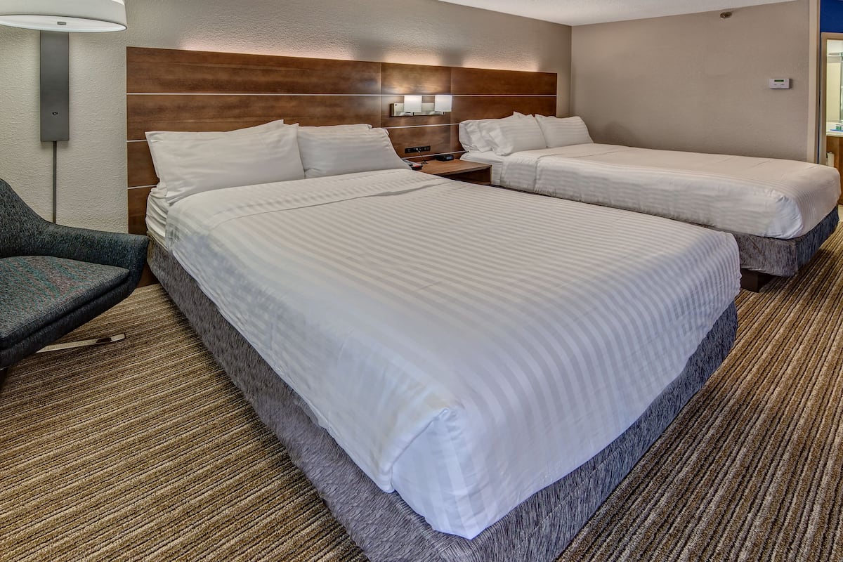 A hotel room with two single beds, a sofa, a small table, and a wall-mounted lamp.