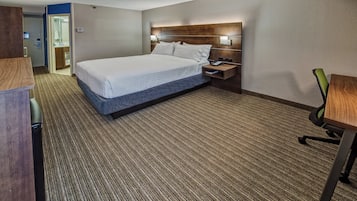 A hotel room with a bed, bedside table, chair, and a desk.