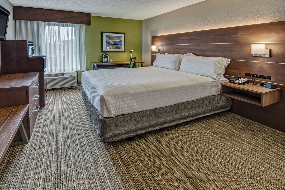 A hotel room with a bed, bedside table, TV, and a window with curtains.