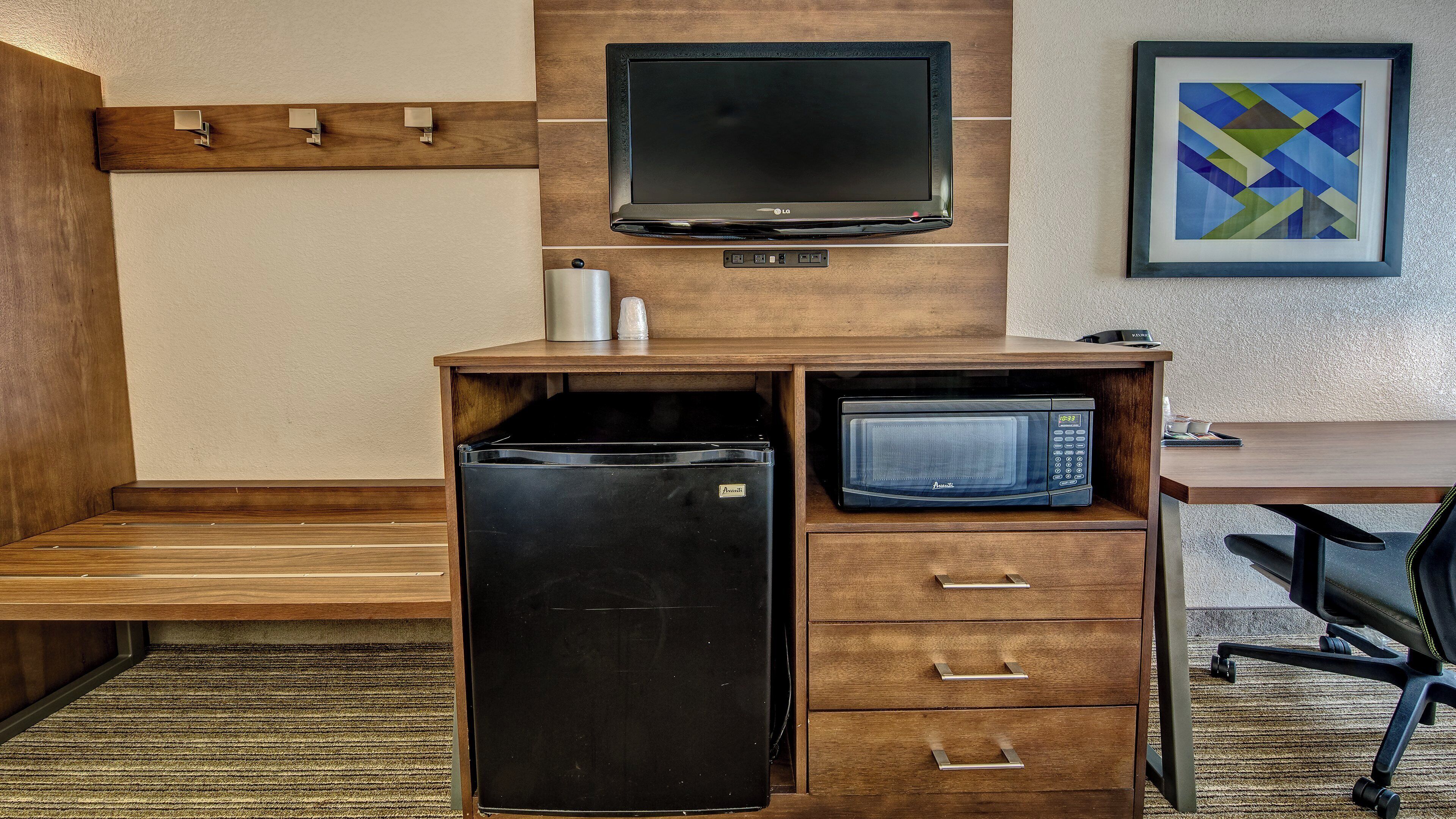 A compact kitchenette with a refrigerator, microwave, and a flat-screen TV.