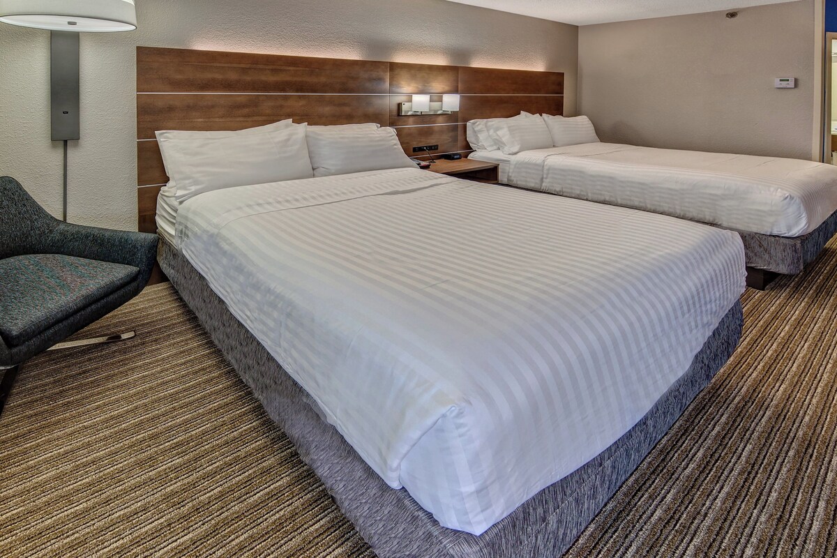 Ein Hotelzimmer mit zwei Betten, einem kleinen Tisch, einem Stuhl und einer Lampe.
