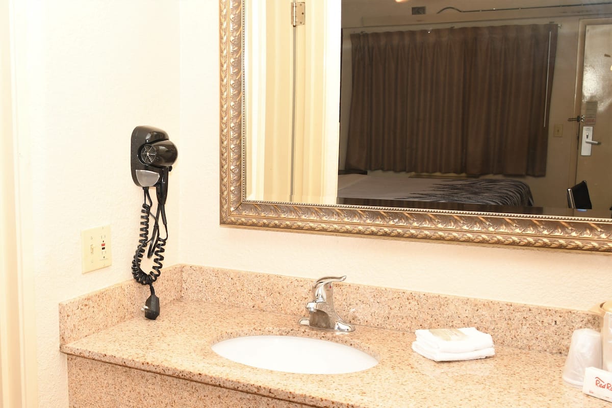 A hotel bathroom with a granite countertop sink, a mirror with an ornate frame, a hair dryer, and a towel dispenser.