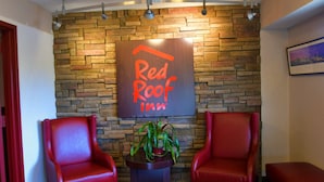A Red Roof Inn sign on a stone wall, two red leather chairs, and a small table with a plant. - Red Roof Inn Richmond South (Richmond)