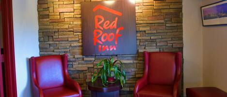 Un letrero de Red Roof Inn sobre un muro de piedra, dos sillones de cuero rojo y una mesita con una planta.