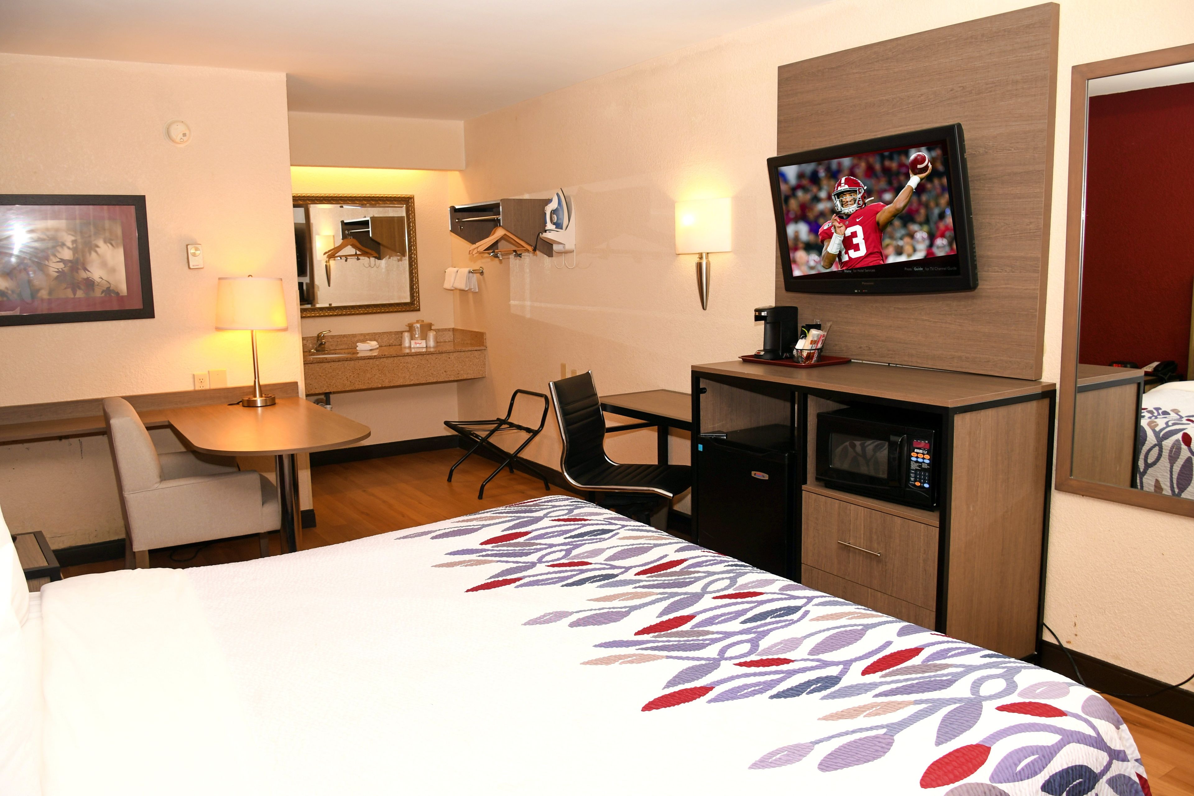 A hotel room with a bed, a desk, a chair, a television, and a microwave.