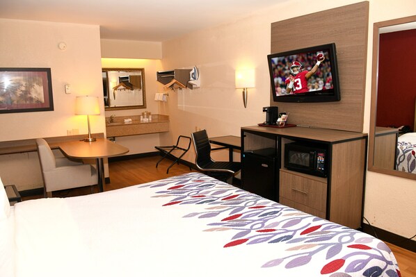 Una habitación de hotel con una cama, un escritorio, una silla, un televisor y un microondas.