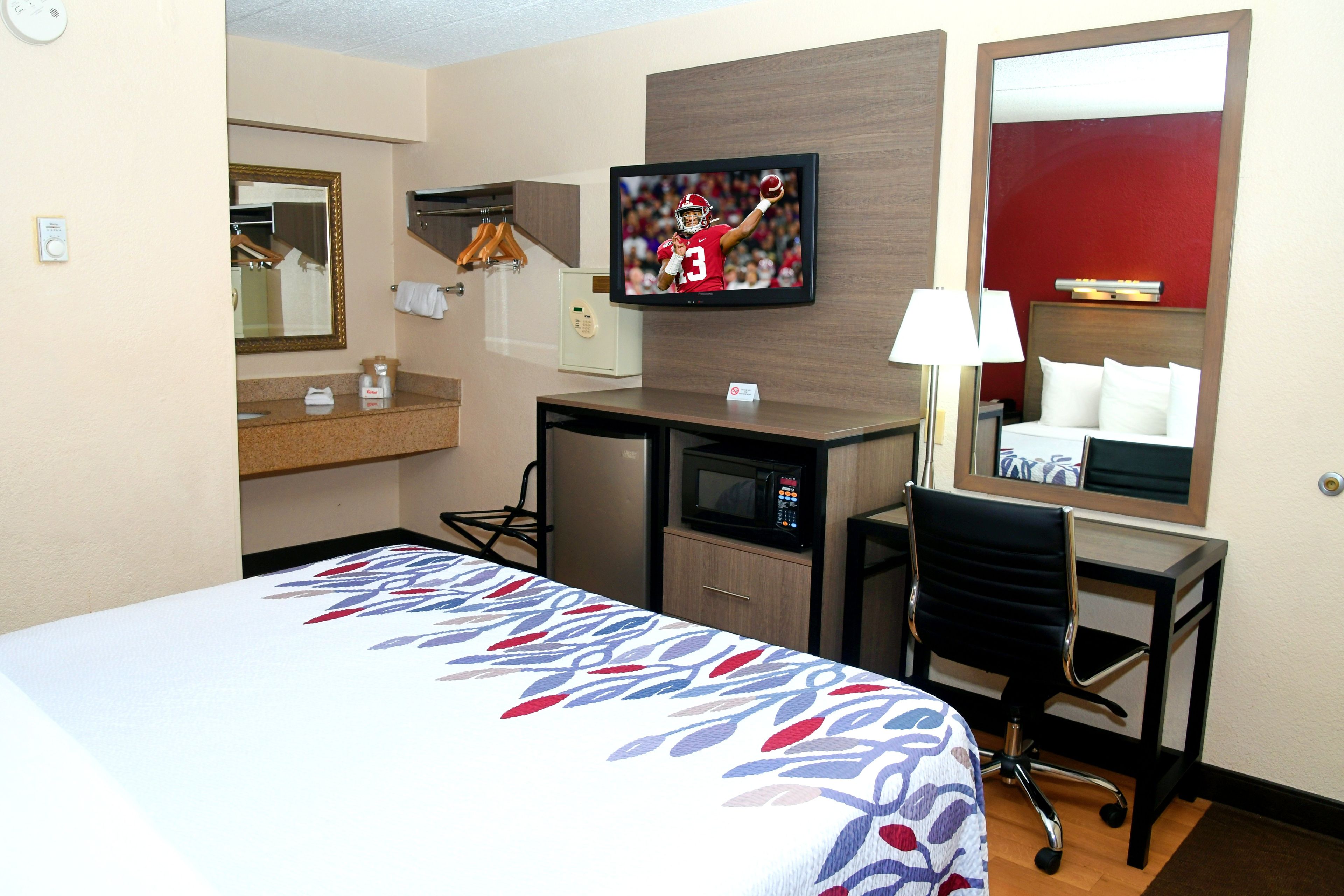 A hotel room with a bed, desk, chair, television, and a mirror.
