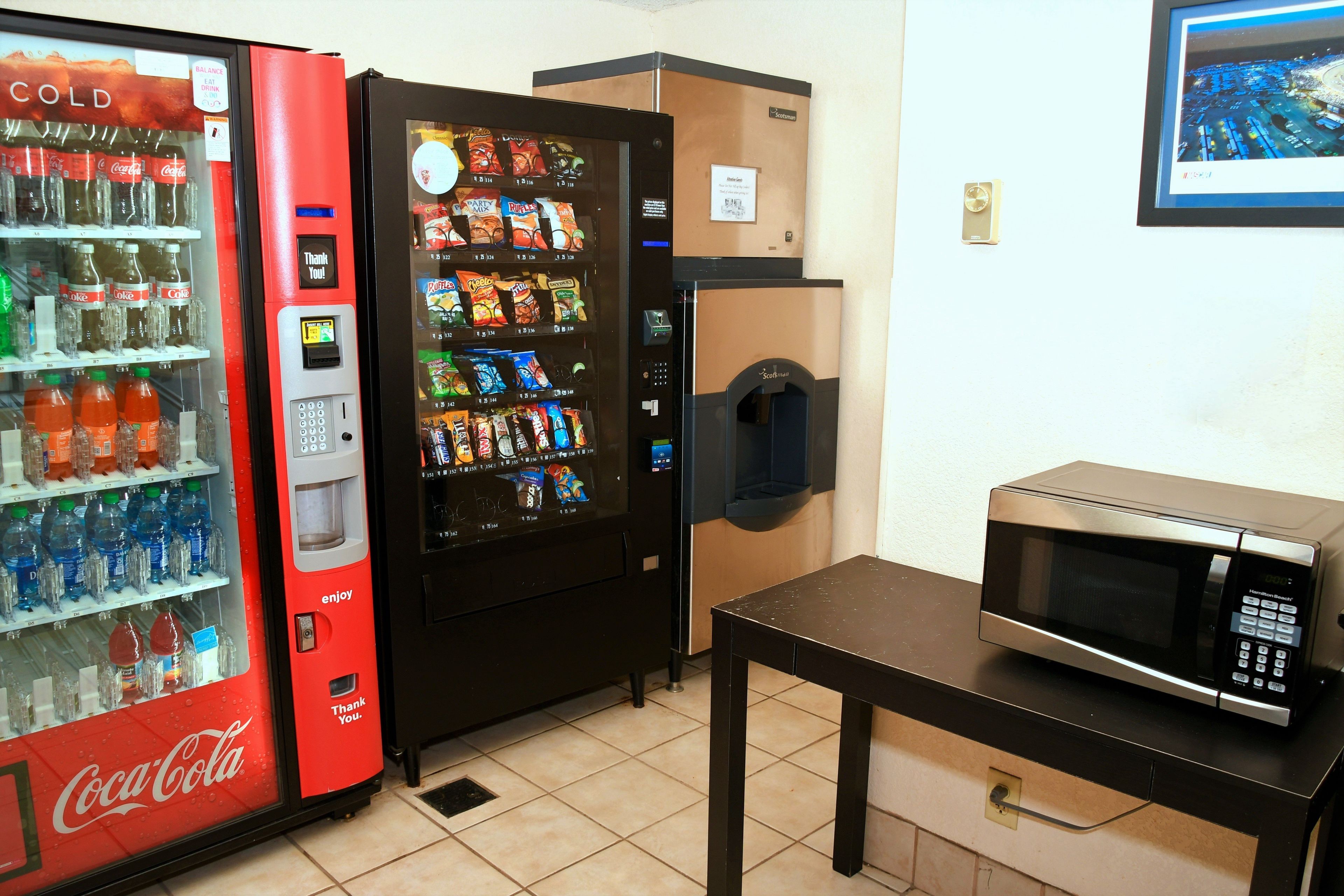 A vending machine area with a Coca-Cola cooler, a snack vending machine, and a microwave on a table.
