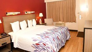 Habitación de hotel con una cama grande, mesitas de noche, un escritorio, una lámpara, un calefactor y una ventana con cortinas.