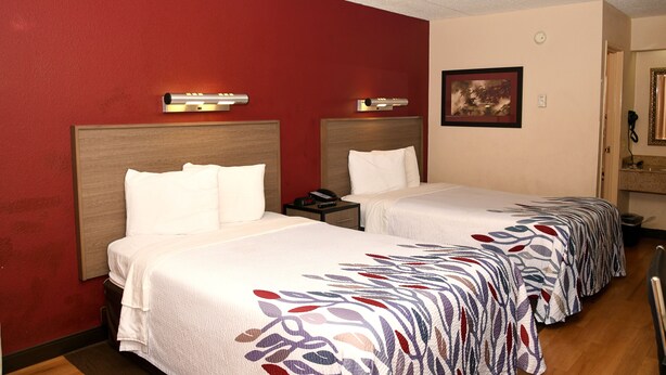 A hotel room with two beds, a red wall, a painting, and a mirror. - Red Roof Inn Richmond South (Richmond)