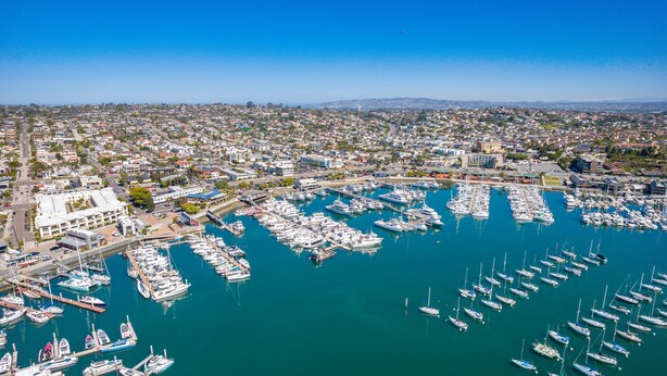 Vista aérea de un puerto deportivo con numerosas embarcaciones amarradas, rodeado por una zona residencial con edificios y calles.
