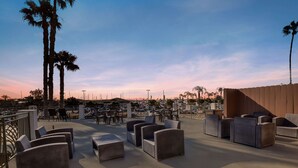 Terraza en la azotea con mobiliario de mimbre y palmeras, con vista a un puerto deportivo.