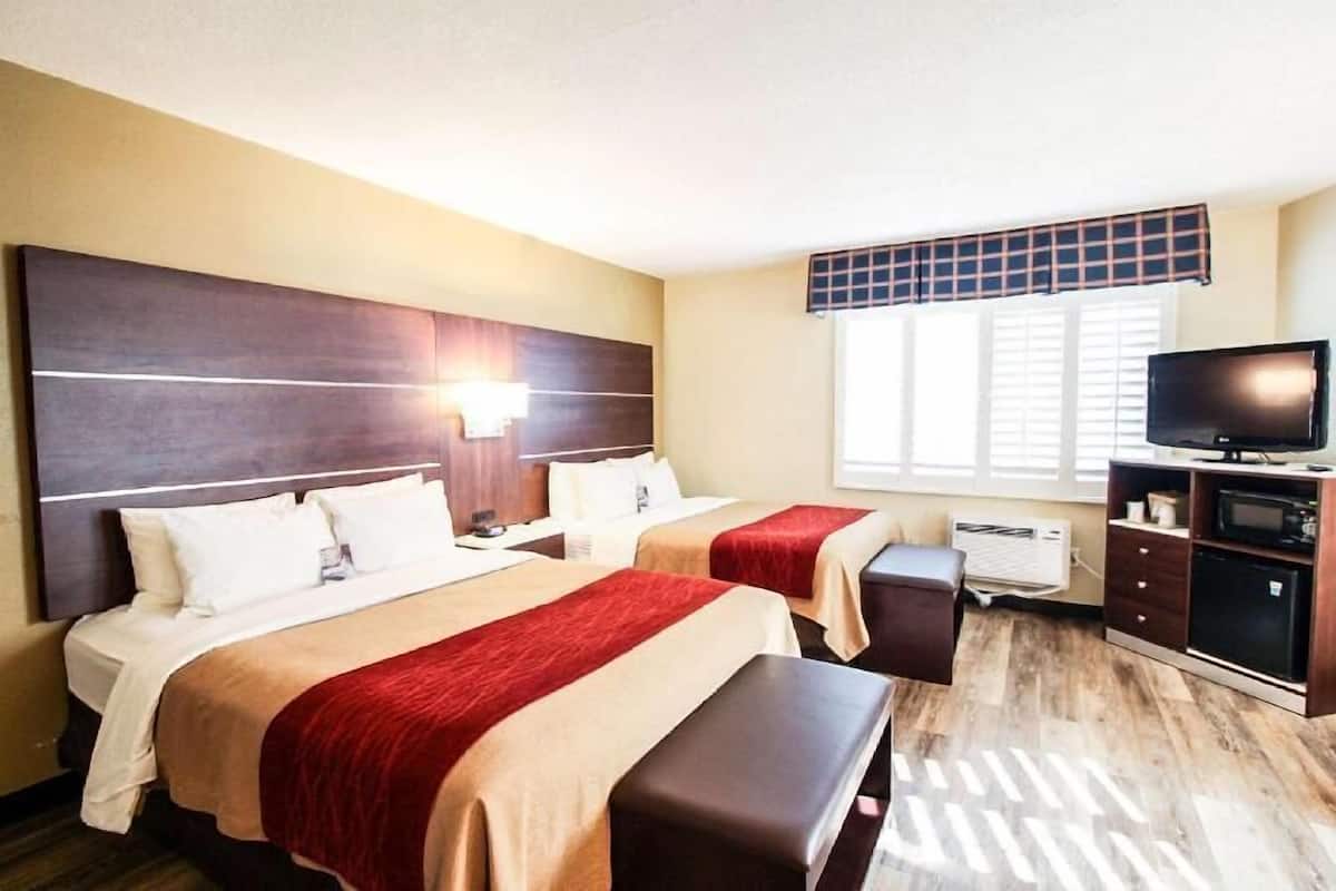 Habitación de hotel con dos camas, televisión, escritorio y ventana.