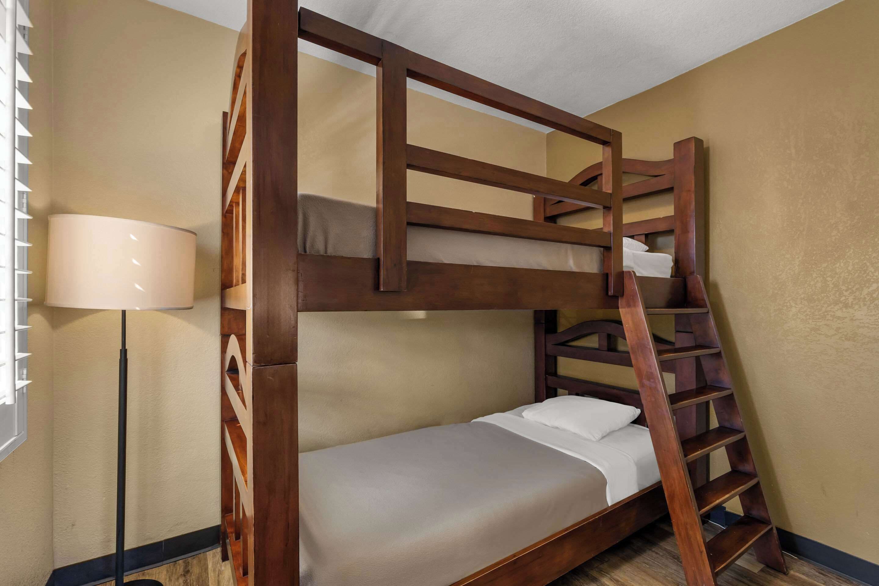 Un lit superposé avec une échelle en bois, une lampe de chevet et un mur uni.