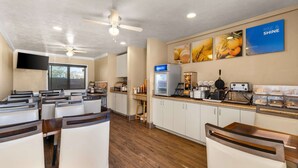 Un restaurante con barra para desayunos, ventiladores de techo y zona de cocina equipada.