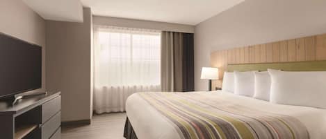 A hotel room with a bed, a TV, a desk, and a window with curtains.