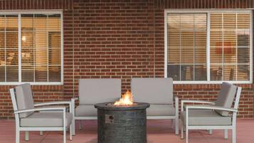 A patio area with a stone fire feature surrounded by white chairs and a gray sofa.