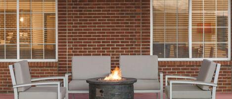 Un espacio de patio con una chimenea de piedra rodeada de sillas blancas y un sofá gris.