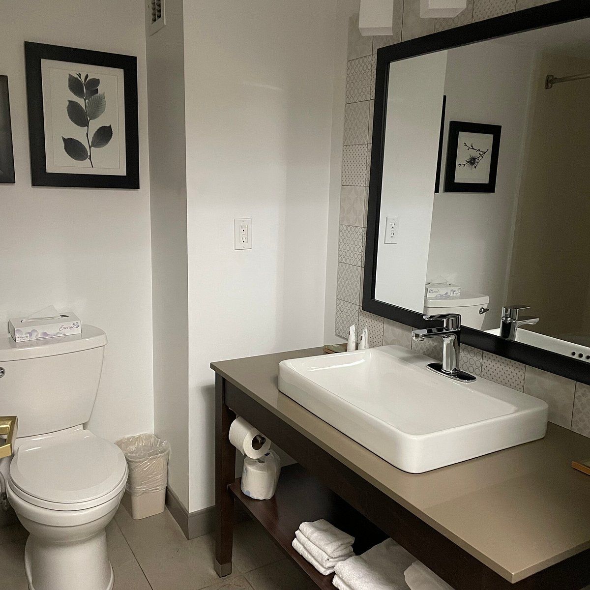 Un baño con inodoro blanco, lavamanos con espejo y un cesto de basura.