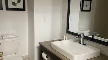 Un baño con inodoro blanco, lavamanos con espejo y un cesto de basura.
